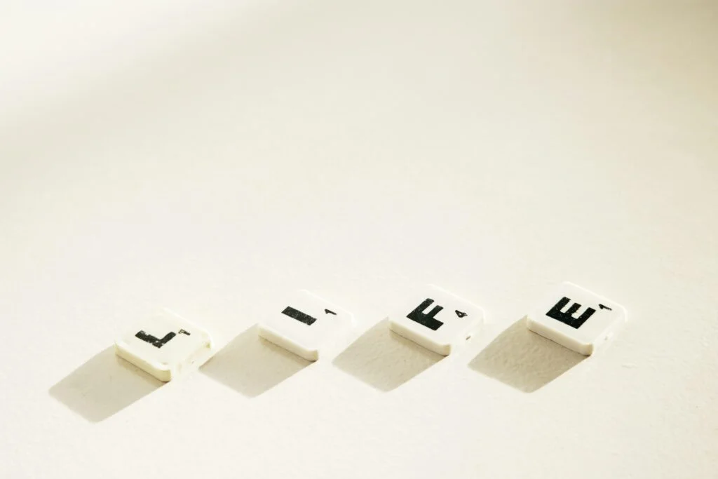 Four white Scrabble tiles with black letters spelling the word "LIFE" are arranged in a horizontal line on a pale surface. Each tile casts a short shadow to the right, symbolizing the foundational importance of Life Insurance in safeguarding your future.