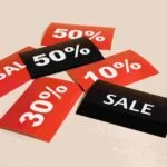 A scattered arrangement of red and black sale tags, displaying various discount percentages (50%, 50%, 30%, and 10%) and the word "SALE," lies against a neutral background. Just like finding the right insurance policy, these tags offer diverse savings to consider.