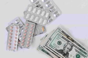 Blister packs of pills are scattered beside a stack of U.S. twenty-dollar bills on a white surface, highlighting the stark contrast between health essentials and financial burdens in today's insurance-driven world.