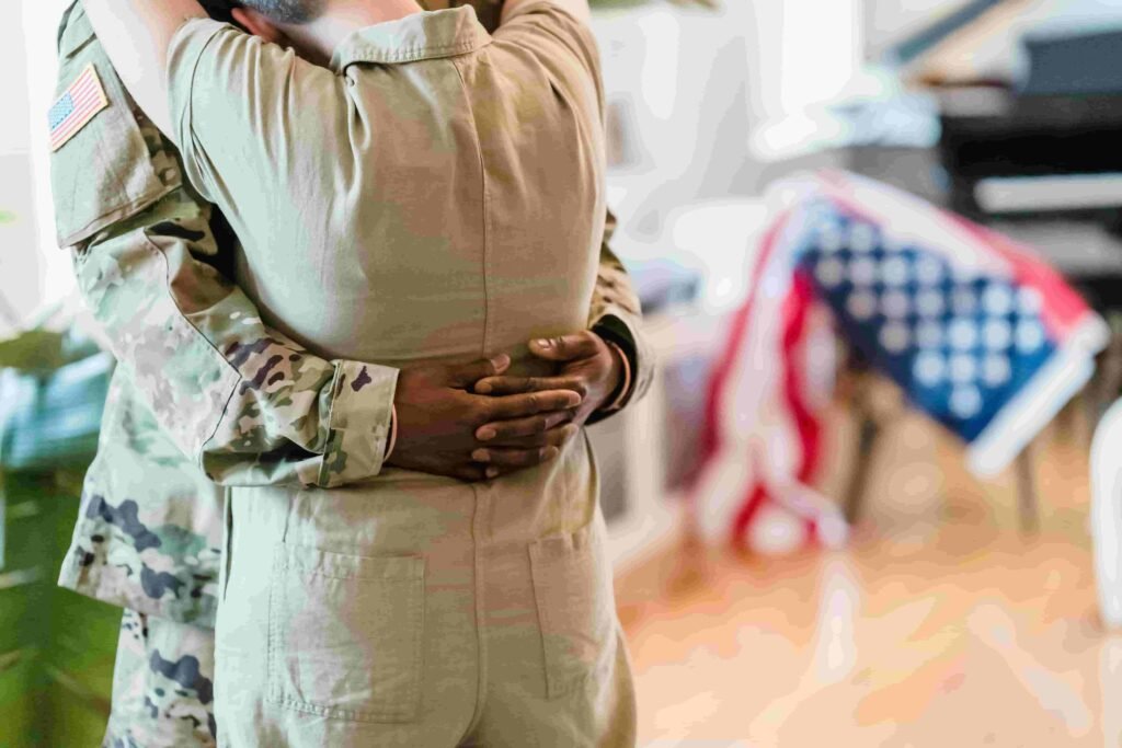 A person in military uniform embraces another indoors, with an American flag partially visible in the background, symbolizing the care and dedication often mirrored in healthcare.