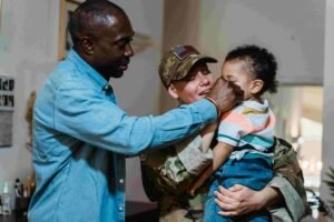 A man in a blue shirt gently touches the face of a young child, cradled in the arms of someone in military uniform. The child's striped shirt and warm smiles suggest a strong sense of family connection, reminiscent of the comforting care found within healthcare environments.