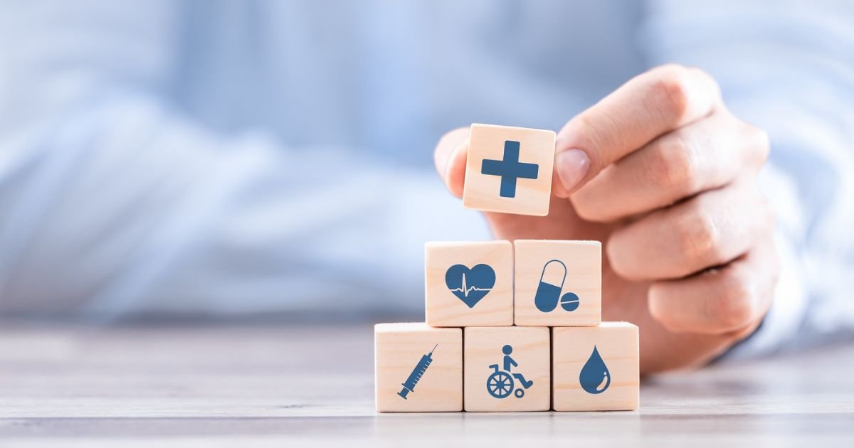 A hand stacks wooden blocks with healthcare icons—cross, heart, pills, syringe, wheelchair, and blood drop—symbolizing different aspects of medical care, much like building a foundation for security such as cheap event insurance in USA California.